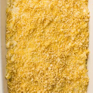 A close-up of an unbaked macaroni and cheese casserole topped with a layer of crushed crackers or breadcrumbs in a white baking dish.