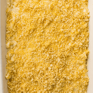 A close-up of an unbaked macaroni and cheese casserole topped with a layer of crushed crackers or breadcrumbs in a white baking dish.