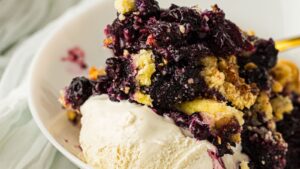 A serving of vanilla ice cream topped with blueberry crumble dessert on a white plate.