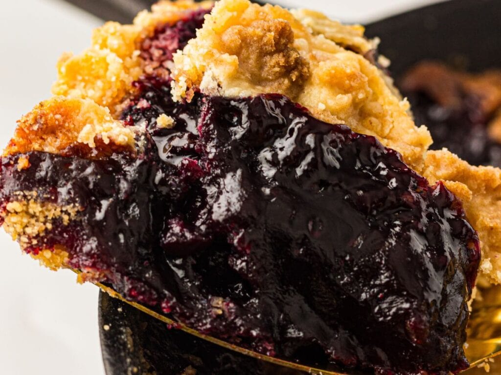 A close-up of a slice of blueberry dump cake showing a golden, crumbly crust and thick, glossy blueberry filling.