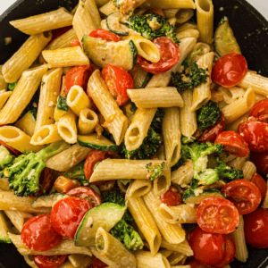 Penne pasta mixed with broccoli, zucchini, and cherry tomatoes in a creamy sauce.