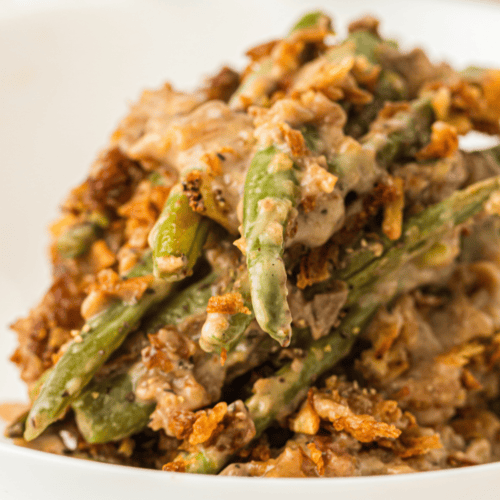 A close-up of green bean casserole with creamy sauce and crispy fried onions served on a white plate.