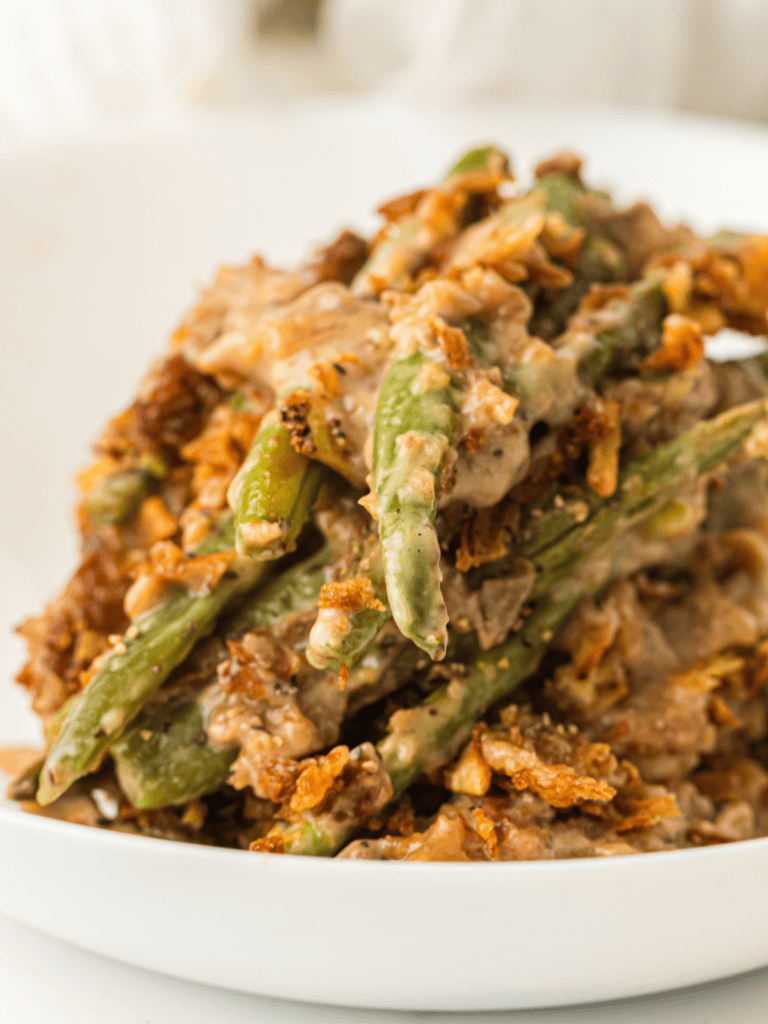 A close-up of green bean casserole with creamy sauce and crispy fried onions served on a white plate.