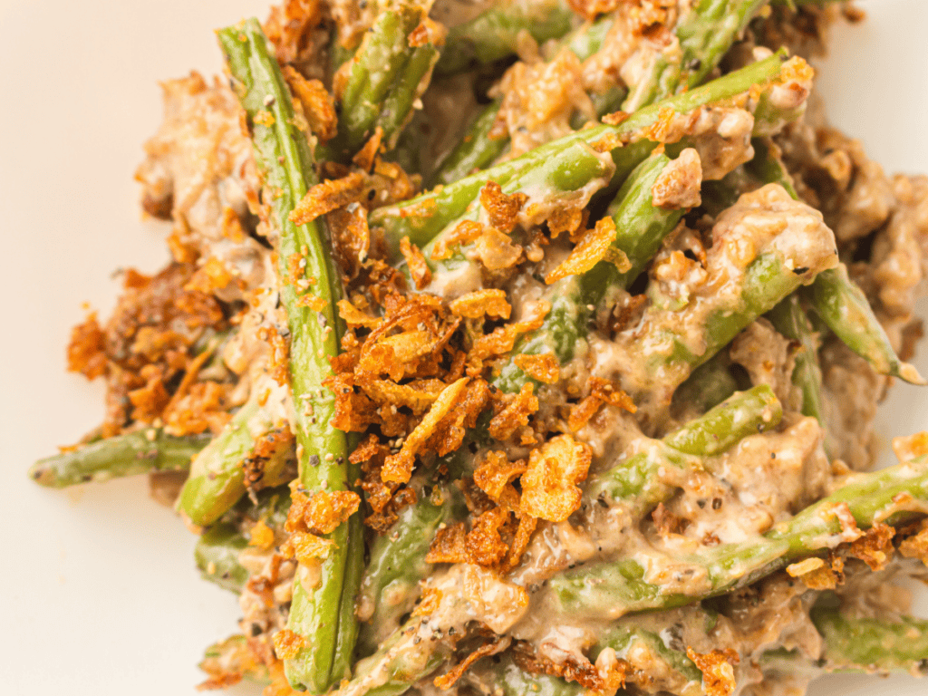 Green bean casserole with creamy sauce and crispy fried onions on top, served on a white plate.