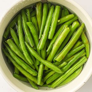 A bowl filled with fresh green beans submerged in water.