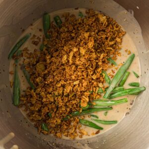 Green beans, creamy sauce, and crispy fried onions in a metal mixing bowl.