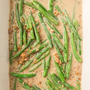 Fresh green beans in a creamy mustard sauce with visible whole grain mustard seeds and spices in a white dish.