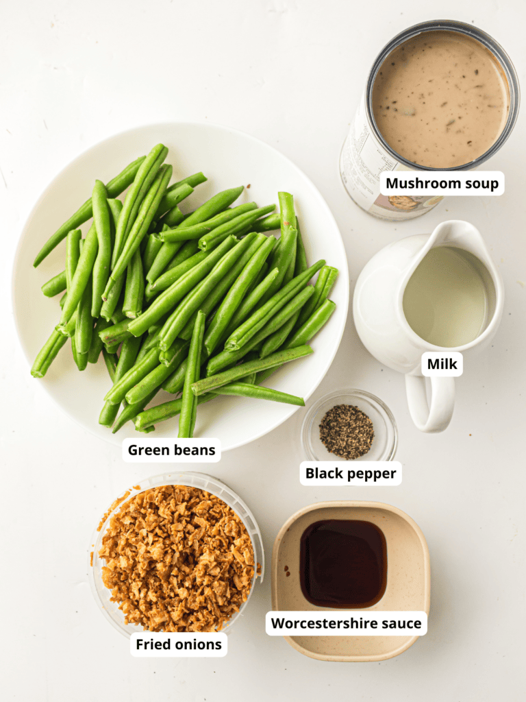 Ingredients for green bean casserole: fresh green beans, mushroom soup, milk, black pepper, fried onions, and Worcestershire sauce, each item labeled on a white background.