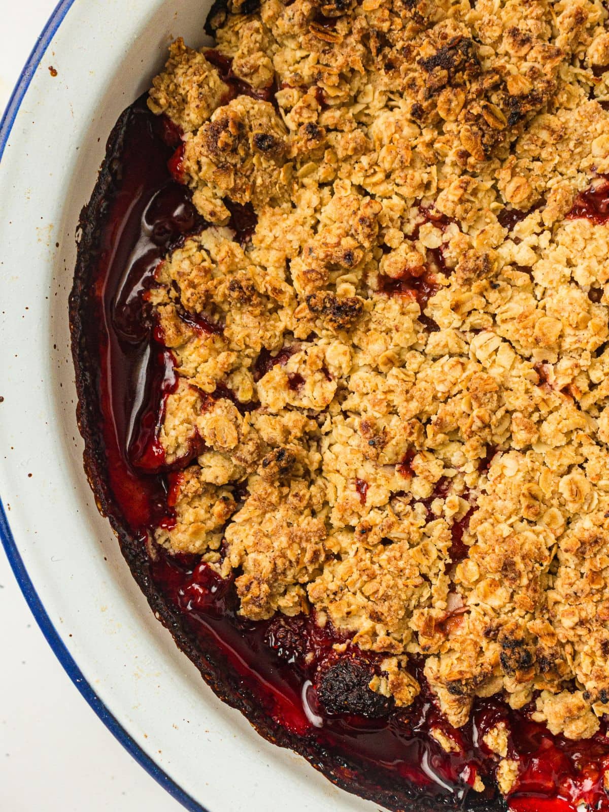 A close-up of a baked strawberry crumble dessert with a golden oat topping and visible red fruit filling in a white dish.
