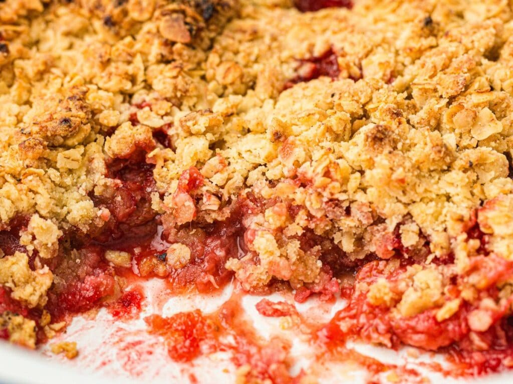 Close-up of a strawberry crumble with a golden oat topping, showing baked fruit filling and crumbly texture.