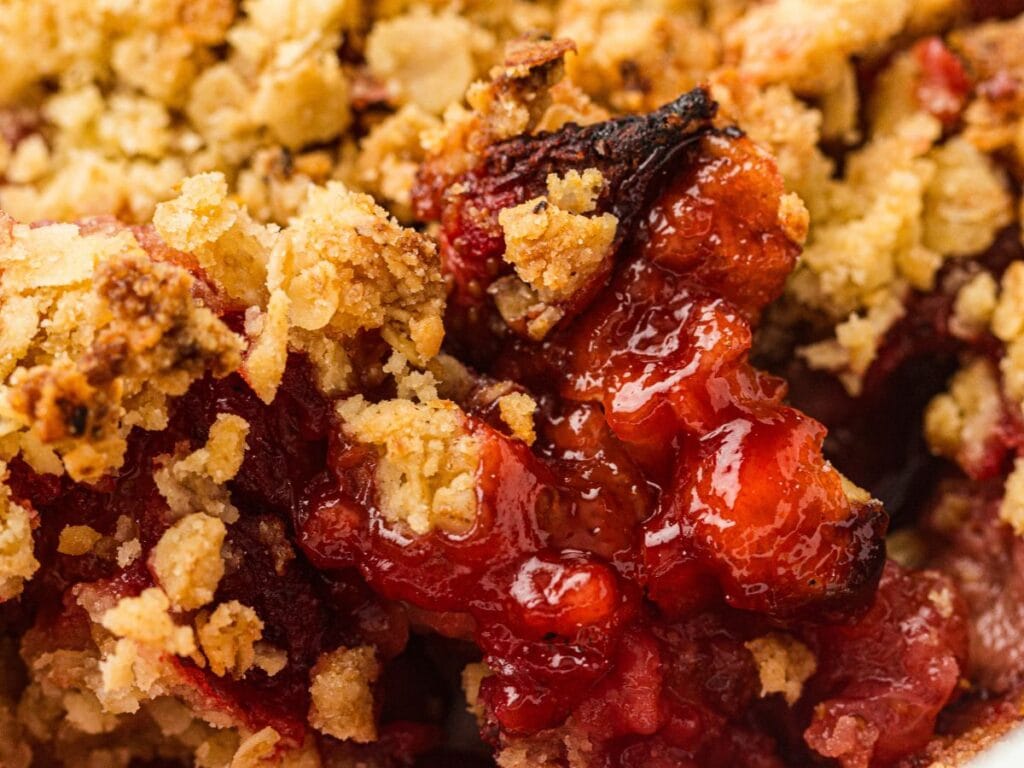 Close-up of a baked fruit crisp dessert with a crumbly golden topping and visible red fruit filling.