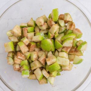 Diced green apples coated with cinnamon and sugar in a clear glass bowl.