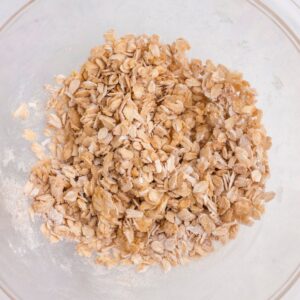 A clear bowl containing a mixture of dry rolled oats and flour sitting on a white surface.