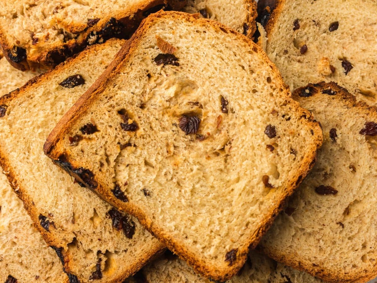 Several slices of raisin bread are stacked in a close-up view, showing pieces of raisins baked into the light brown bread.