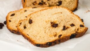 Two slices of raisin bread are placed on a white surface, showing a golden-brown crust and raisins baked into the soft interior.