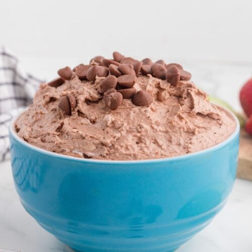 A blue bowl filled with chocolate mousse, topped with chocolate chips, sits on a white surface.