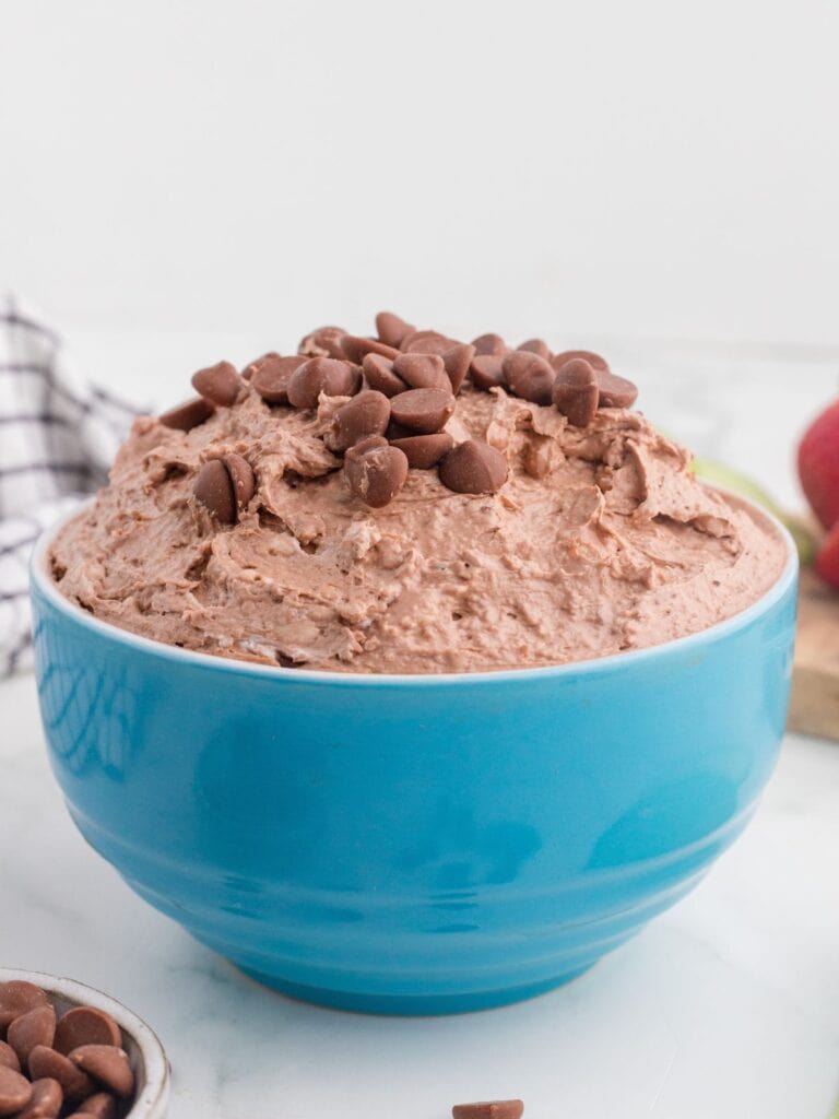 A blue bowl filled with chocolate mousse, topped with chocolate chips, sits on a white surface.