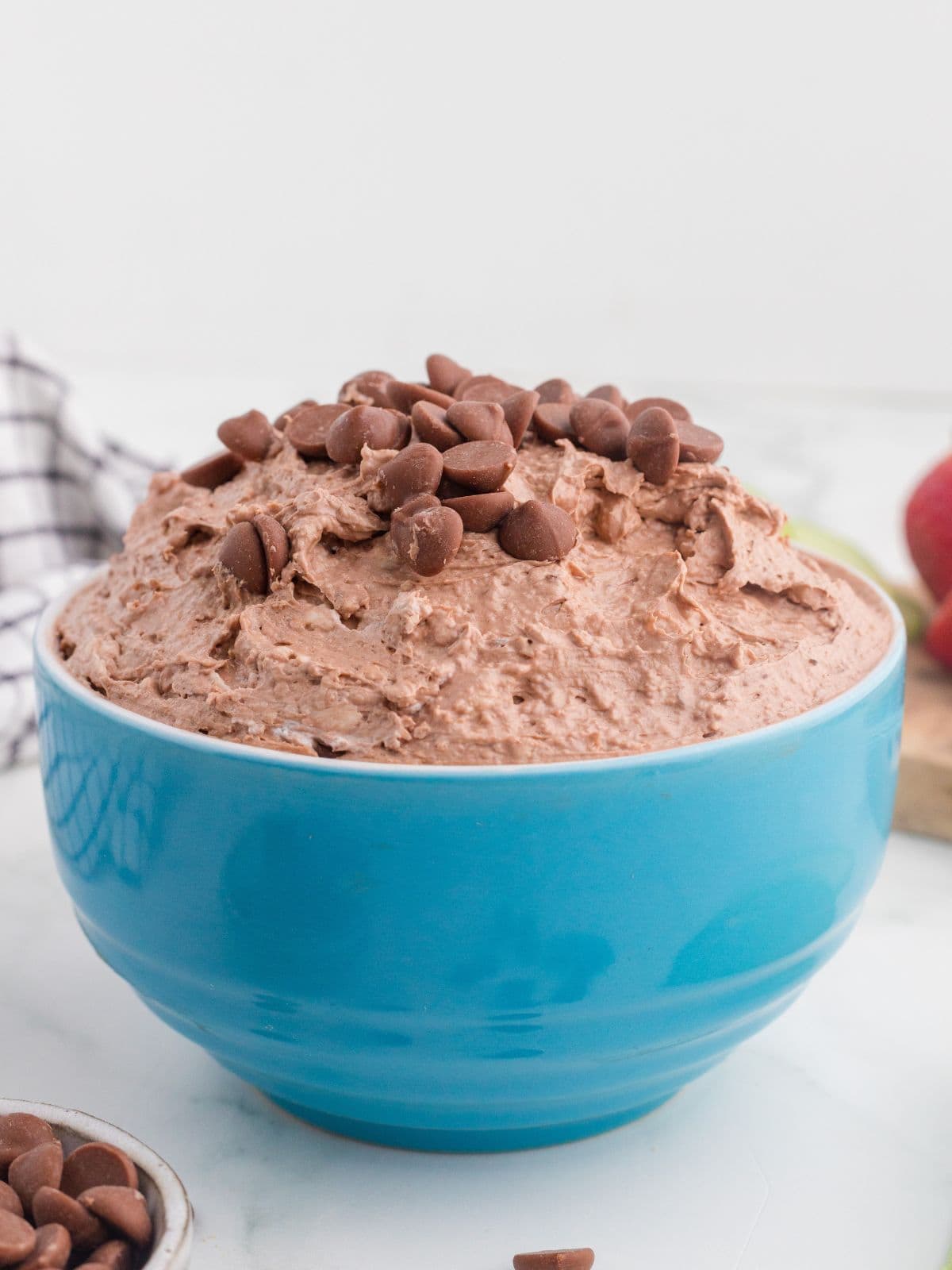 A blue bowl filled with chocolate mousse, topped with chocolate chips, sits on a white surface.