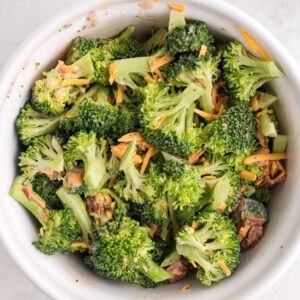 A bowl of broccoli salad mixed with shredded cheese and pieces of bacon.