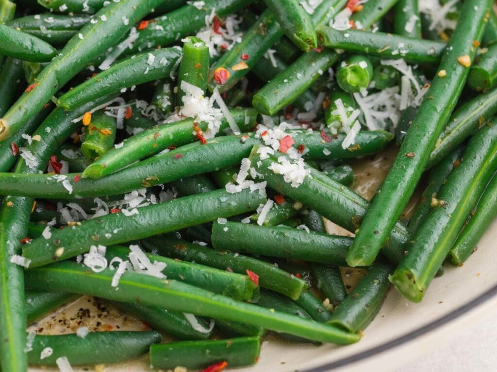 Close-up of cooked green beans topped with grated cheese and red pepper flakes.