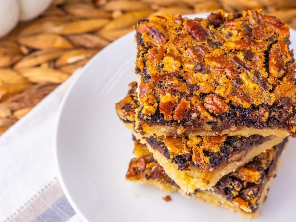 A stack of three chocolate pecan bars on a white plate.