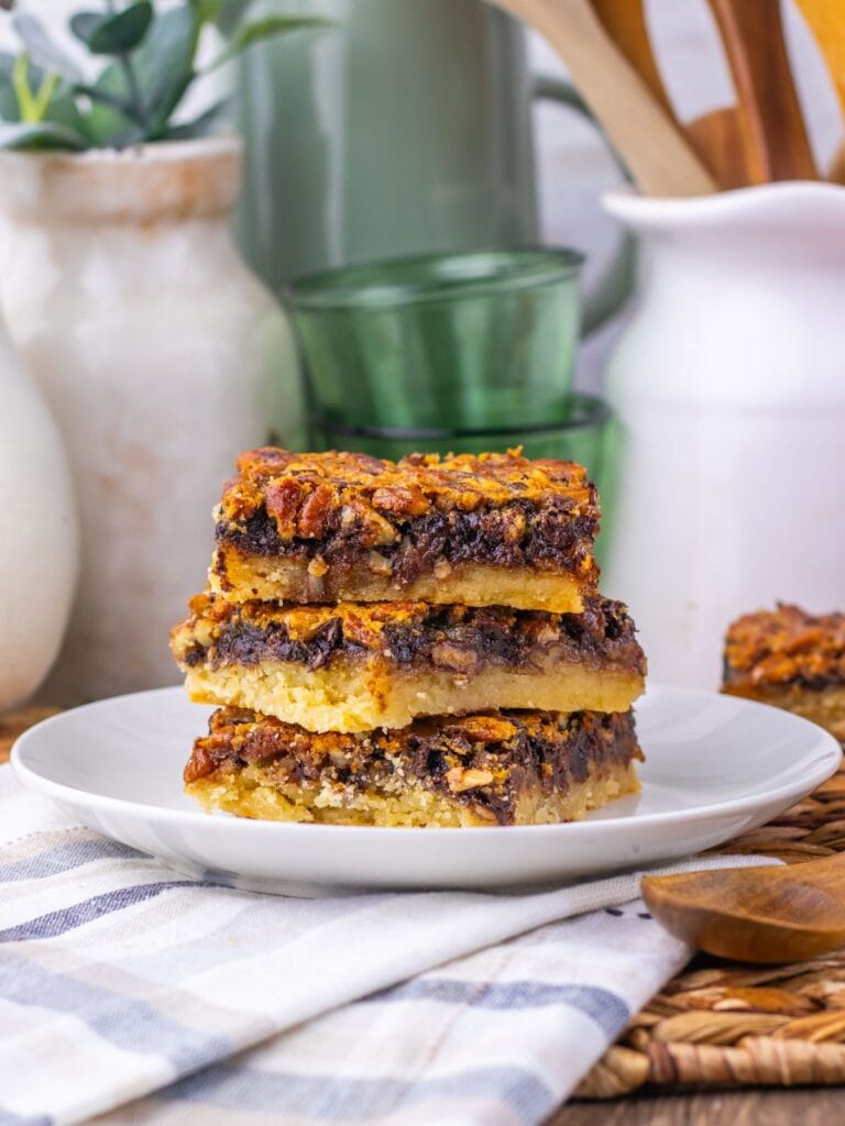 A stack of three pecan pie bars on a white plate.