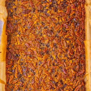 A tray of baked pecan and chocolate chip bars lined with parchment paper.