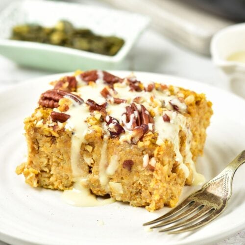 A square of baked oatmeal topped with pecans and drizzled with icing on a white plate with a fork.