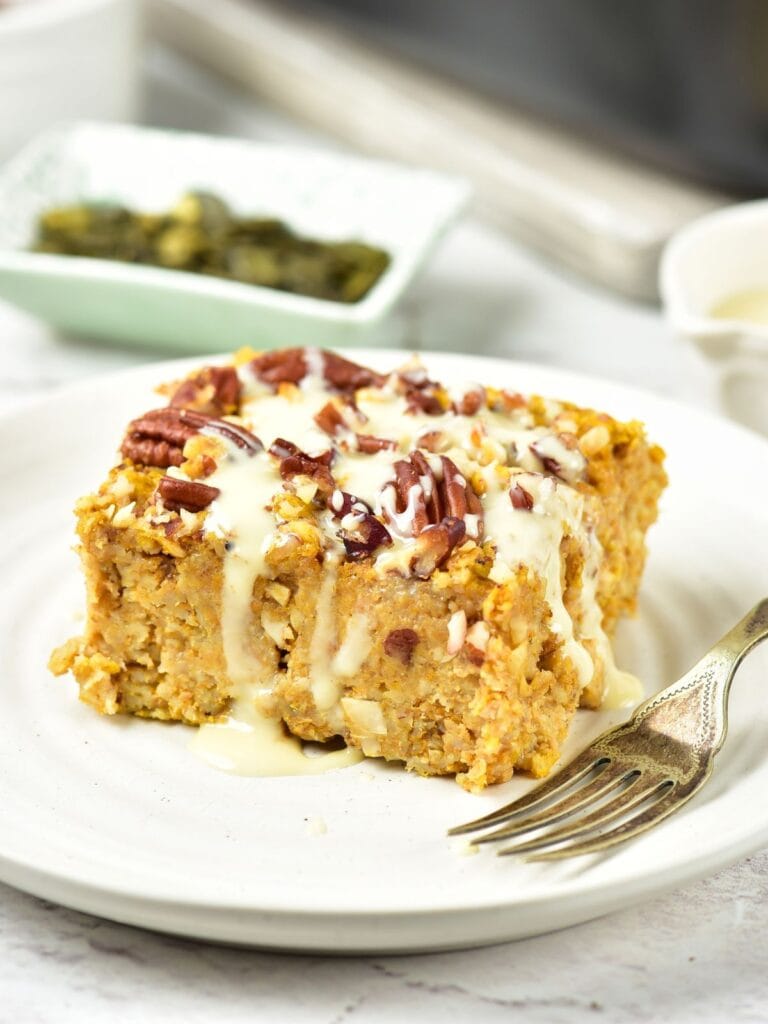 A square of baked oatmeal topped with pecans and drizzled with icing on a white plate with a fork.