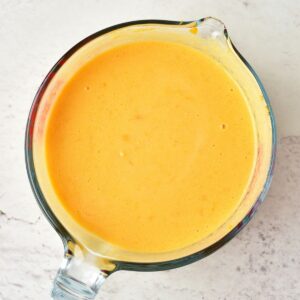 A glass measuring cup filled with orange-colored puréed soup.