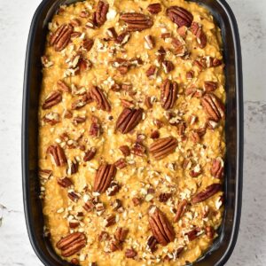 Unbaked pumpkin casserole in a rectangular baking dish, topped with pecan halves and chopped nuts.