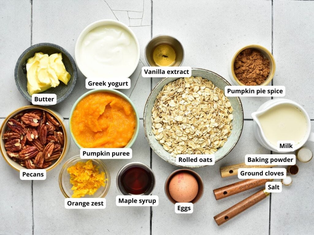 Overhead view of bowls containing ingredients for pumpkin oatmeal, including oats, pumpkin puree, yogurt, pecans, an egg, and spices, each labeled with its name.