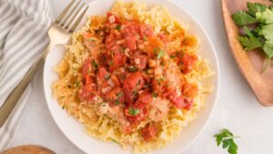 Chicken topped with tomato sauce and herbs served over ruffled pasta in a white bowl.