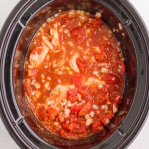 Chicken pieces simmering in a tomato and onion sauce inside a slow cooker.