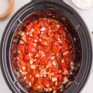 Slow cooker filled with diced tomatoes and chopped onions.
