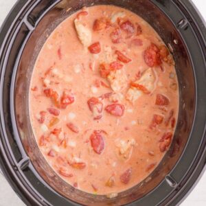 A creamy tomato and chicken mixture cooking in a slow cooker.