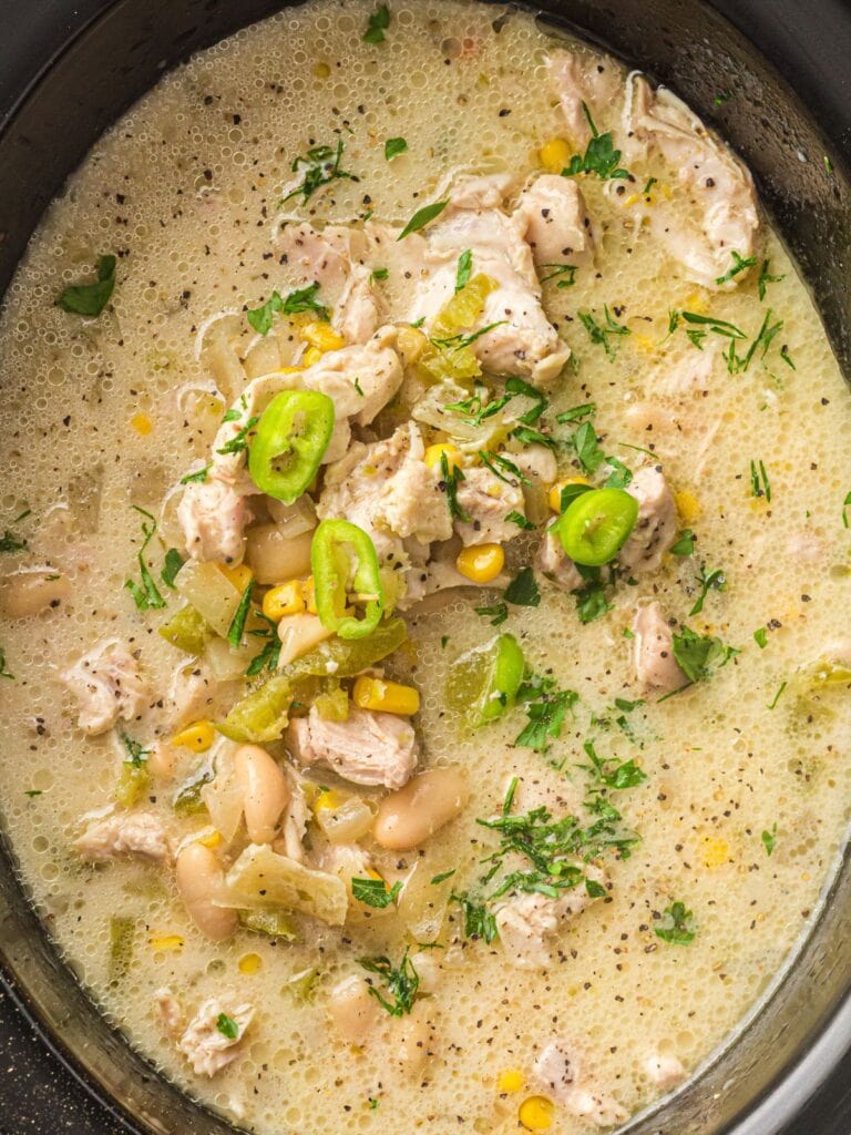 Creamy white chicken chili with white beans, corn, and sliced jalapeños in a slow cooker.