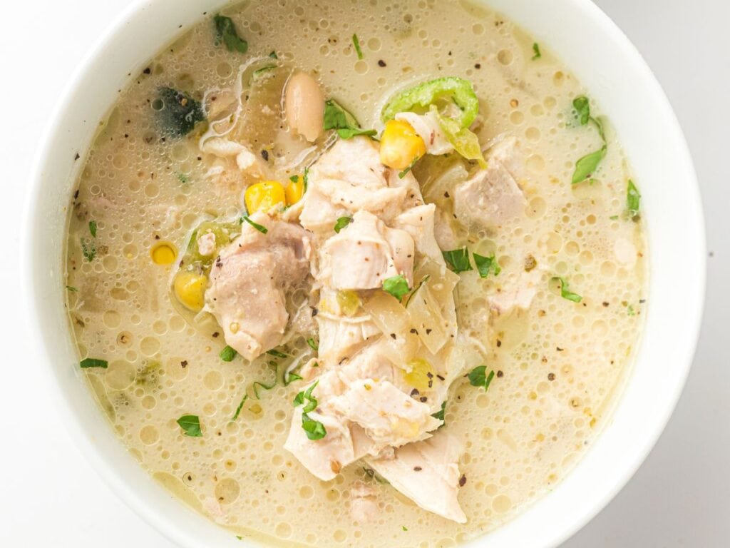 A bowl of chicken white bean chili with corn and herbs.