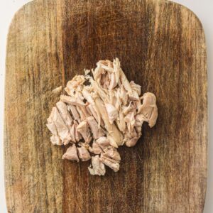 A pile of shredded cooked chicken on a wooden cutting board.