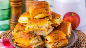 A stack of turkey and cheese slider sandwiches on a plate next to a red apple.