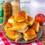 A pile of small, turkey and cheese sliders on a ceramic plate.
