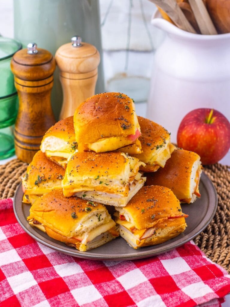 A pile of small, turkey and cheese sliders on a ceramic plate.