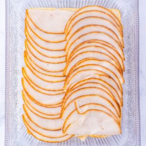 Sliced turkey deli meat layered over bread in a glass baking dish.