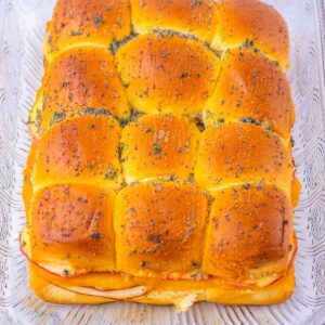 A rectangular pan of baked ham and cheese sliders topped with poppy seeds.